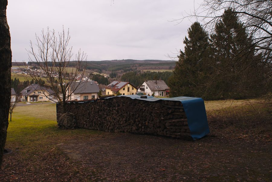 Vue sur Neuhütten depuis un sentier vers le Dollberg avec une pile de bois au premier plan