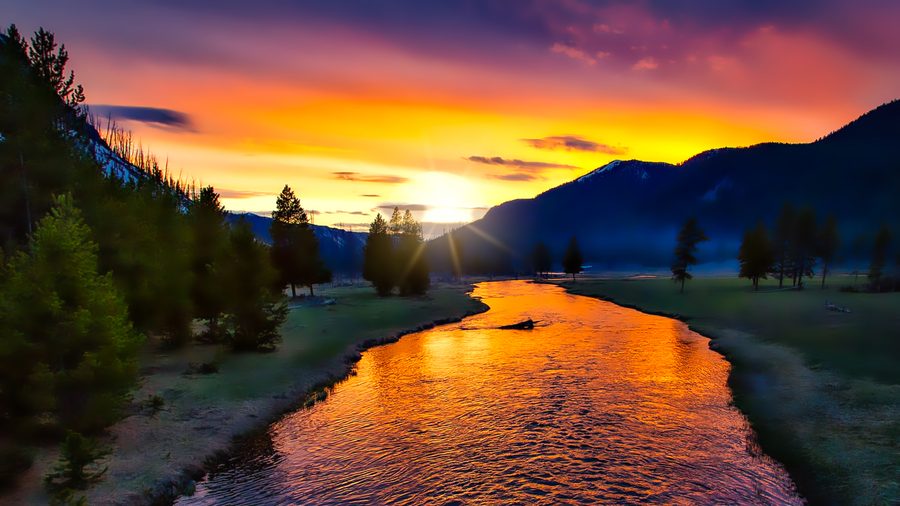 Coucher de soleil au-dessus du parc national de Yellowstone avec une lumière chaude et des nuages au-dessus du paysage.
