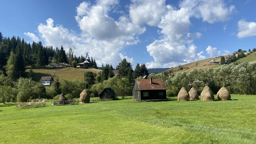Village de Poiana Horea avec meules de foin, église et cimetière dans les monts Apuseni