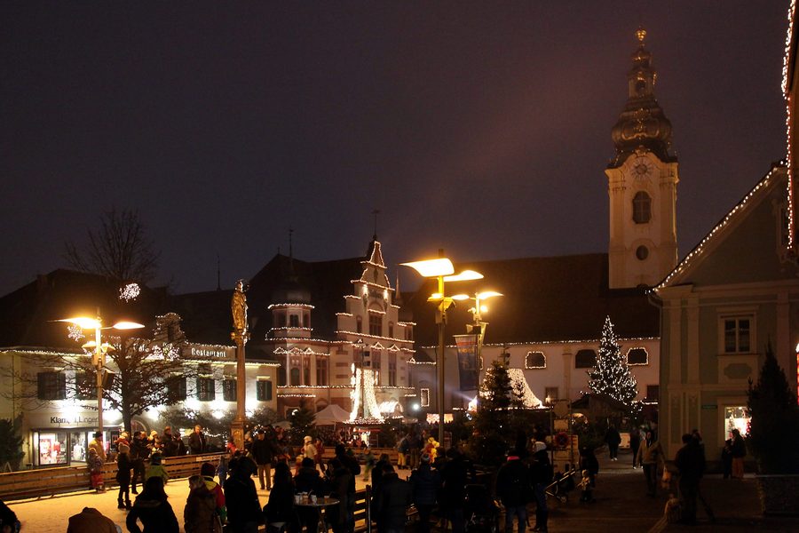 Place principale de Hartberg éclairée avec bâtiments historiques, colonne mariale, hôtel de ville et église paroissiale Saint-Martin